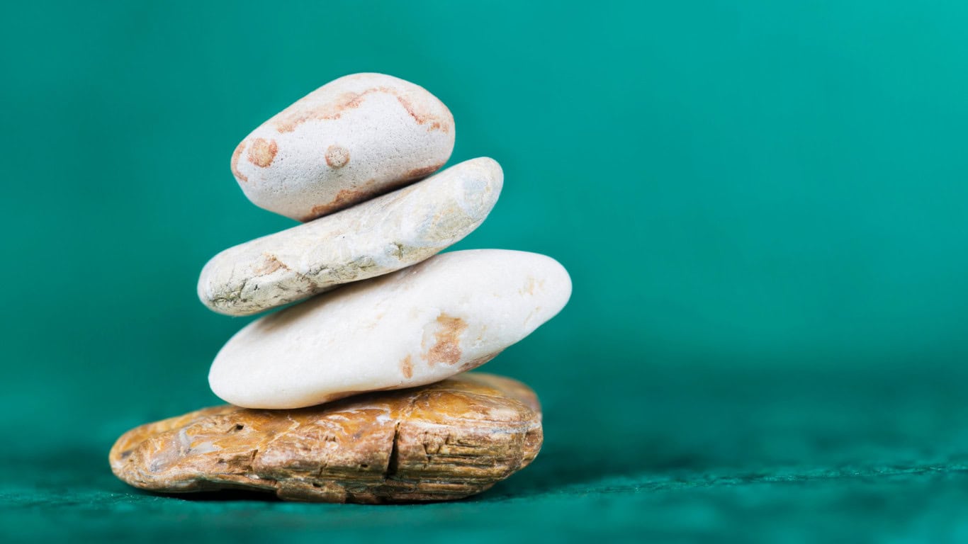 A stack of four balanced stones in focus with a blurry turquoise background.